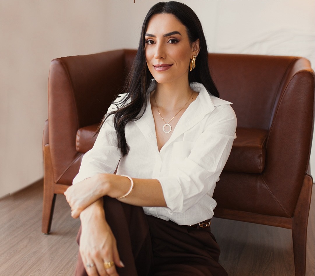 Dra. Carolina Kaplan sorrindo, sentada em uma poltrona da clínica